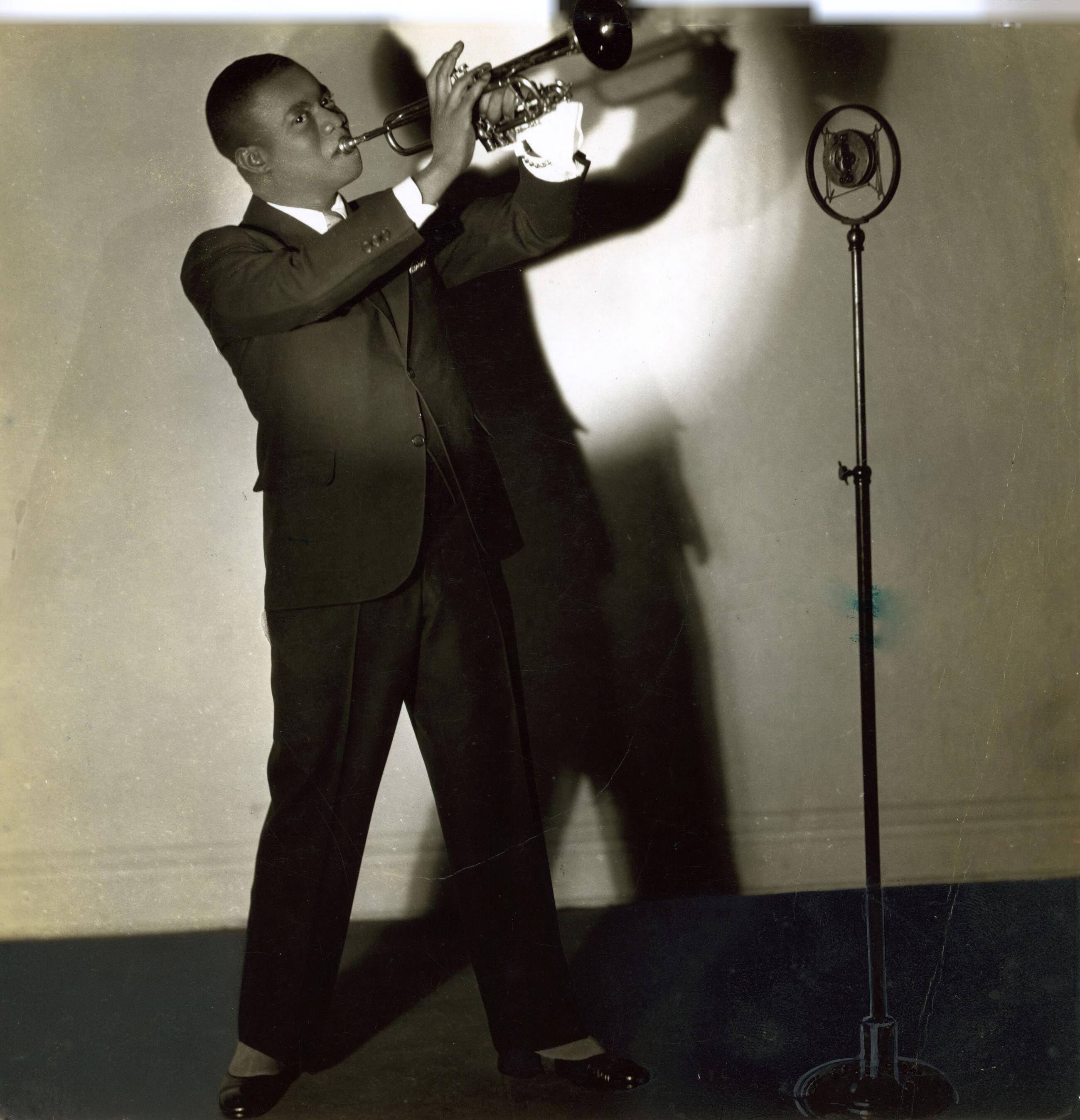 De Amerikaanse trompettist en jazzmuzikant Louis Armstrong achter de microfoon, 1933. Fotograaf onbekend, Collectie Nationaal Archief