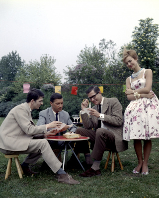 Drie heren spelen een spelletje in de openlucht in het bijzijn van een verleidelijke vrouw met lampionnetjes op de achtergrond, Nederland, circa 1961. Fotograaf Walter Blum / Collectie Spaarnestad
