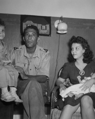 Een KNIL-militair zit samen met een vrouw en twee kinderen in een kamer