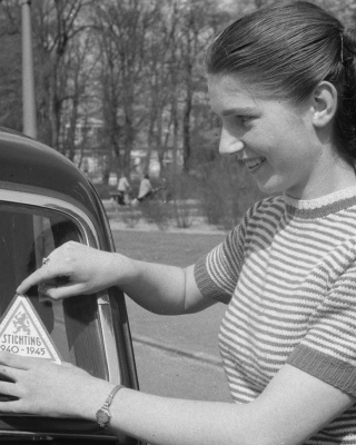 Vrouw plakt sticker Stichting 1940-1945 op auto 