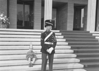 Koningin Juliana opent het nieuwe stadhuis te Vlissingen. Een jongetje met feestmuts zit op de trappen van het bordes van het stadhuis. Voor hem staat een marechaussee, 1965. Foto Jac. de Nijs, Nationaal Archief / Collectie Anefo
