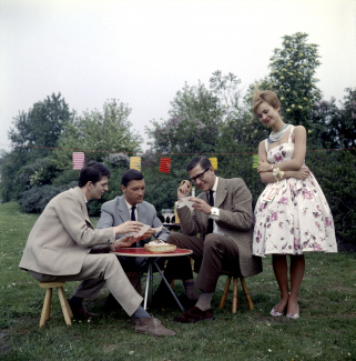 Drie heren spelen een spelletje in de openlucht in het bijzijn van een verleidelijke vrouw met lampionnetjes op de achtergrond, Nederland, circa 1961. Fotograaf Walter Blum / Collectie Spaarnestad